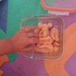 A child's hand reaches into a glass container of orange playdough.