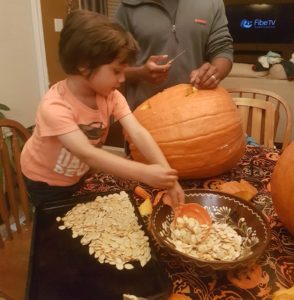 A young child scoops seeds from a pumpkin and spreads them on a baking sheet