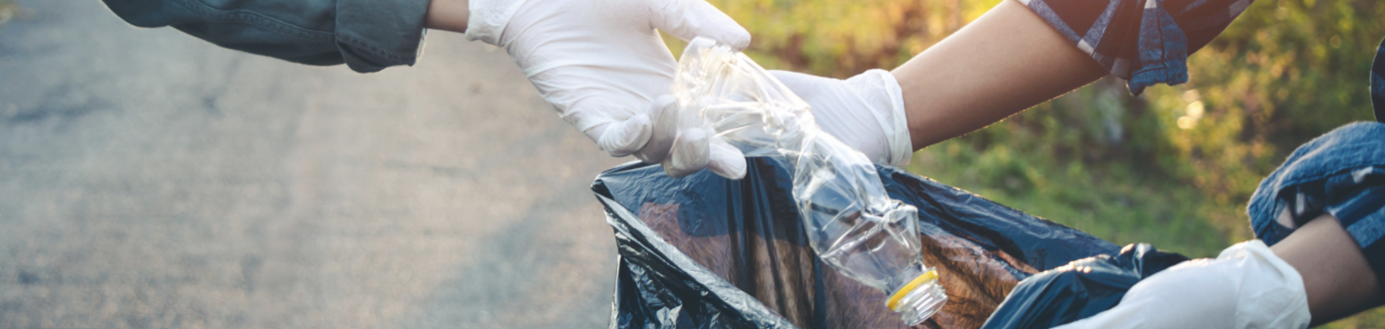 gloved hands putting a crumpled water bottle into a garbage bag