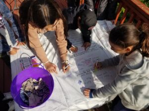 children use markers to answer prompts about sustainable fashion on an upcycled old white sheet
