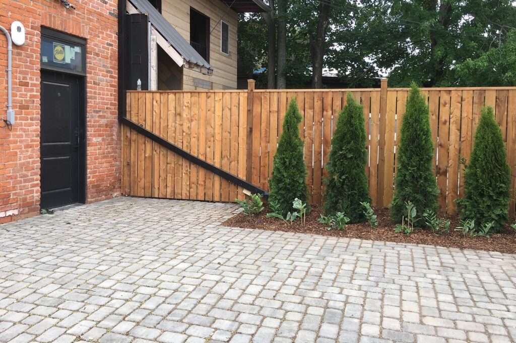A rain spout leads into a garden by a fence in front of a permeable stone paved driveway