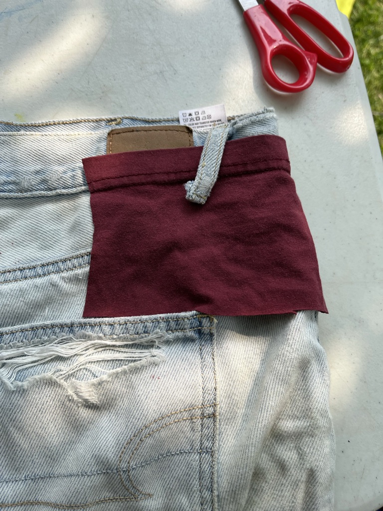 [ID: Red fabric patch placed over shorts. The belt loop of the shorts has been detached and lays over the patch]