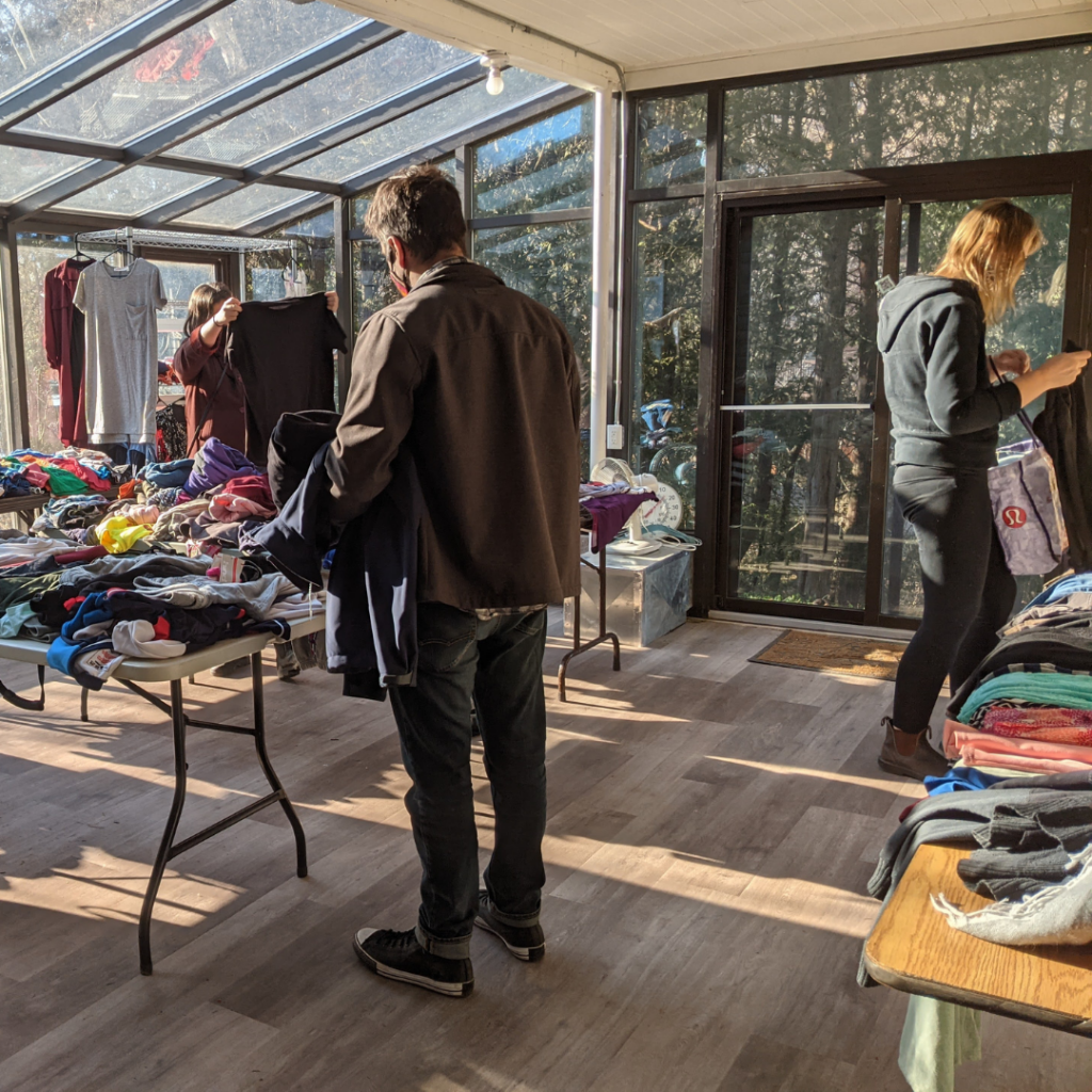Several people look at clothes spread out around the Ecohouse Solarium at the community clothing swap