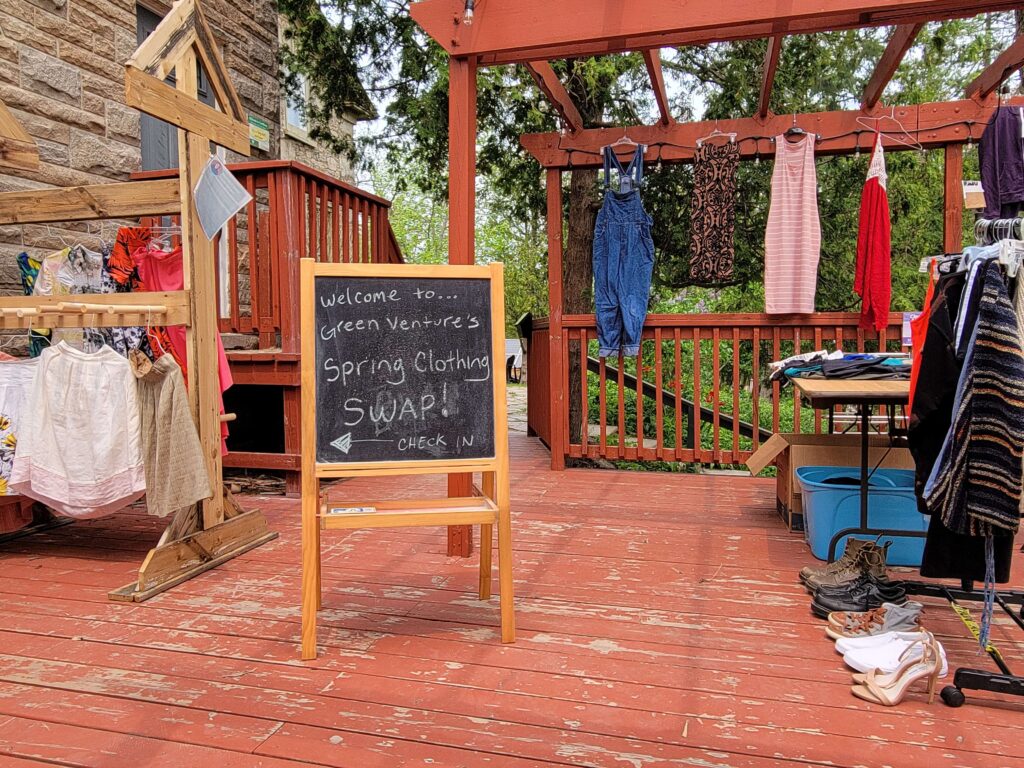 A welcome sign to the community clothing swap at Ecohouse with clothes hung on the deck