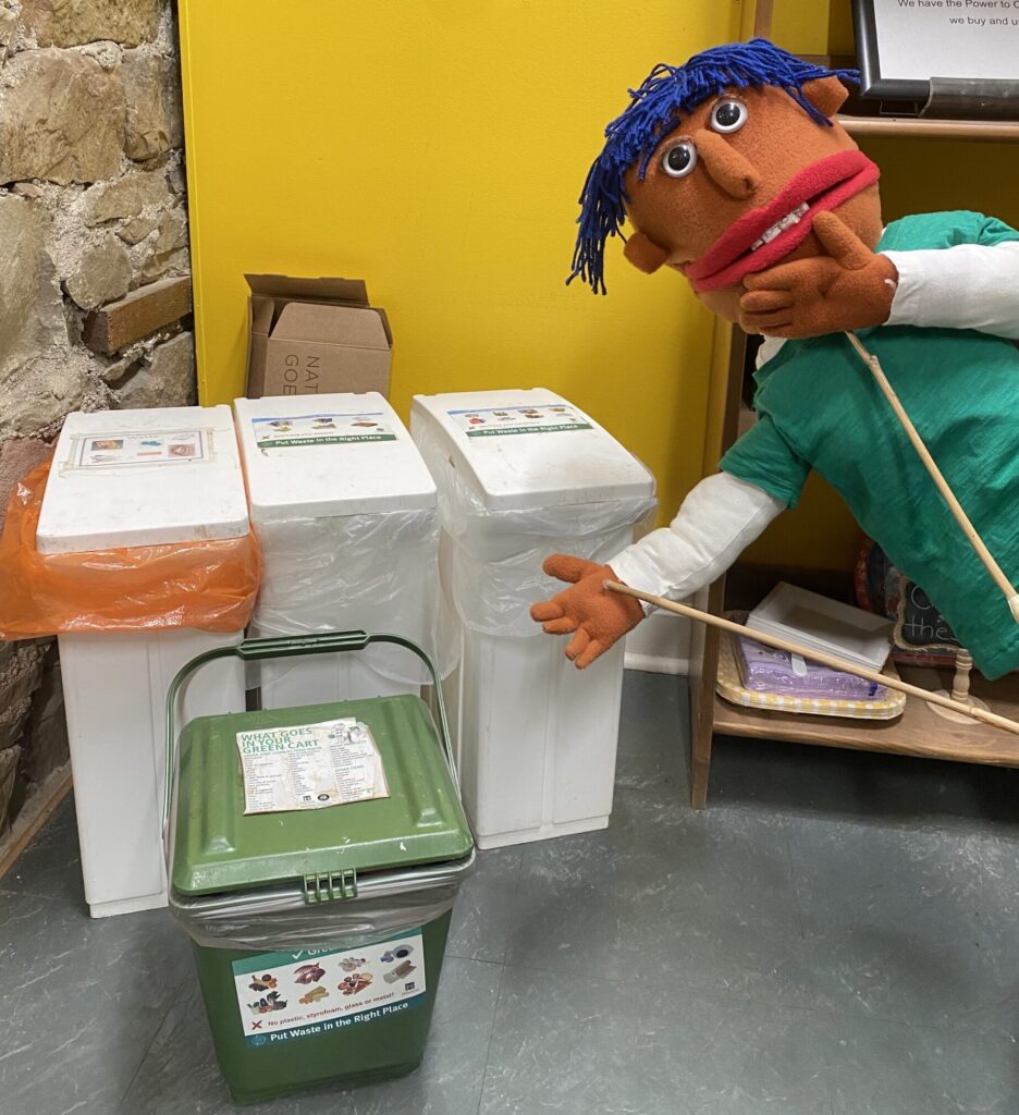 Our puppet kid-in-residence River gestures to several waste containers with a hand on their chin